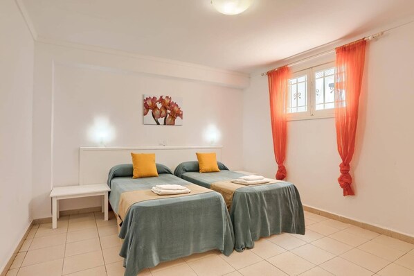 A room with two beds, a bench, and a window with curtains.