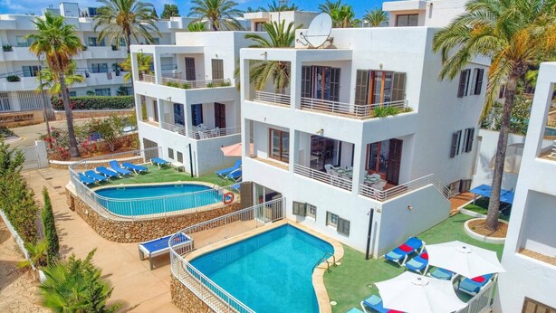 Un hotel a più piani con area piscina, comprensiva di una piscina principale e una più piccola, circondata da lettini e ombrelloni.