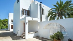 Una moderna casa bianca su due piani con un balcone, una palma e una pianta in vaso.