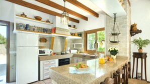 Una cocina con encimeras de granito, vigas de madera y una isla grande con fruta y bebidas.