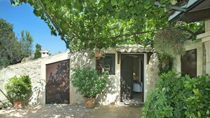 Un edificio de piedra con un porche cubierto, plantas en macetas y una puerta que da a un espacio interior.