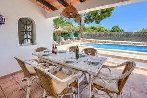 An outdoor dining area with a table set for six, surrounded by wicker chairs with cushions.