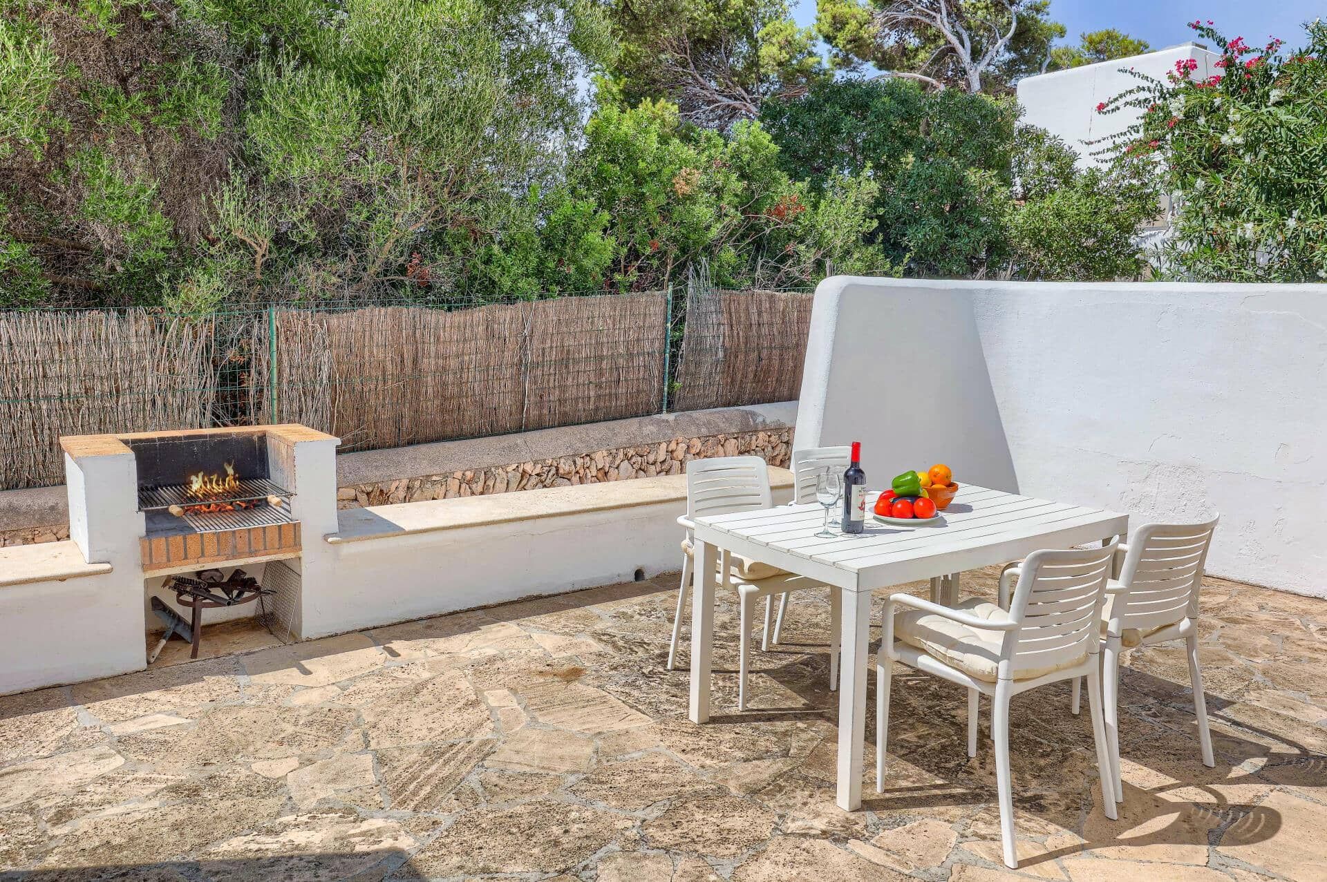Een terras buiten met een barbecue, een tafel met stoelen en een schaal fruit.