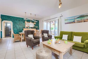 A living room with a green sofa, two armchairs, a wooden coffee table with breakfast items, and a painting of a beach scene.