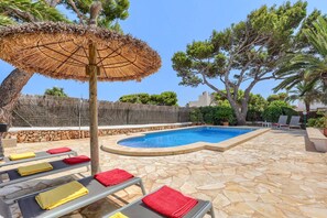 A swimming pool with a stone deck, lounge chairs with towels, and a thatched umbrella.