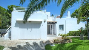 A white building with a covered entrance, a small balcony, and a stone pathway leading to the entrance. - Villa Reco by Villa Plus (Felanitx)