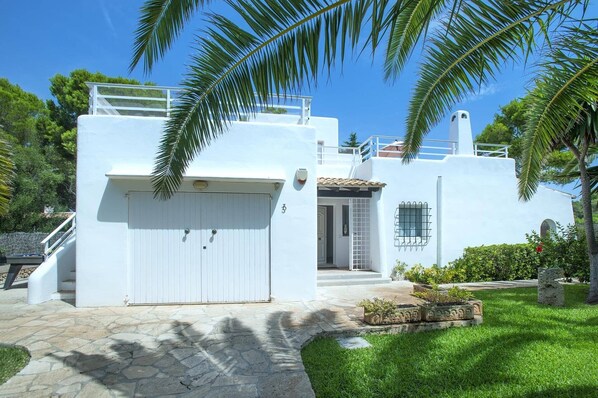 A white building with a covered entrance, a small balcony, and a stone pathway leading to the entrance. - Villa Reco by Villa Plus (Felanitx)