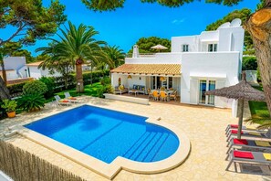 A swimming pool with a sun terrace, lounge chairs, and a covered seating area.
