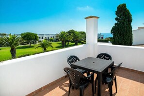 Une terrasse avec une table et des chaises, un pilier blanc et une vue sur un paysage verdoyant avec des bâtiments visibles au loin.