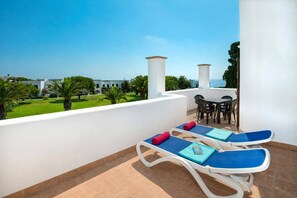 Un balcon avec deux fauteuils, une table et des chaises, donnant sur un paysage verdoyant et une étendue d’eau.