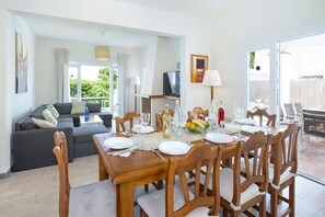 A dining area with a table set for four, a sofa, and a television in the background. - Villa Roca Viva by Villa Plus (Cala d'Or)