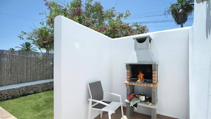 An outdoor patio with a built-in brick grill, a white chair, and a stone wall.