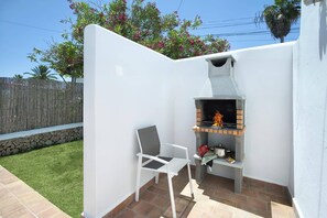 An outdoor patio with a built-in brick grill, a white chair, and a stone wall. - Villa Roca Viva by Villa Plus (Cala d'Or)