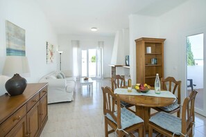 A well-lit living room with a sofa, a dining table with chairs, a wooden cabinet, and a bookshelf. - Villa Roca Viva by Villa Plus (Cala d'Or)