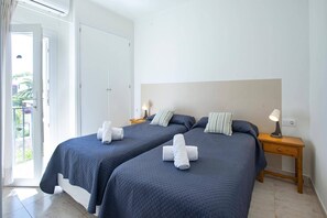 Une chambre d’hôtel avec deux lits, une porte donnant sur un balcon et une table de chevet avec une lampe.