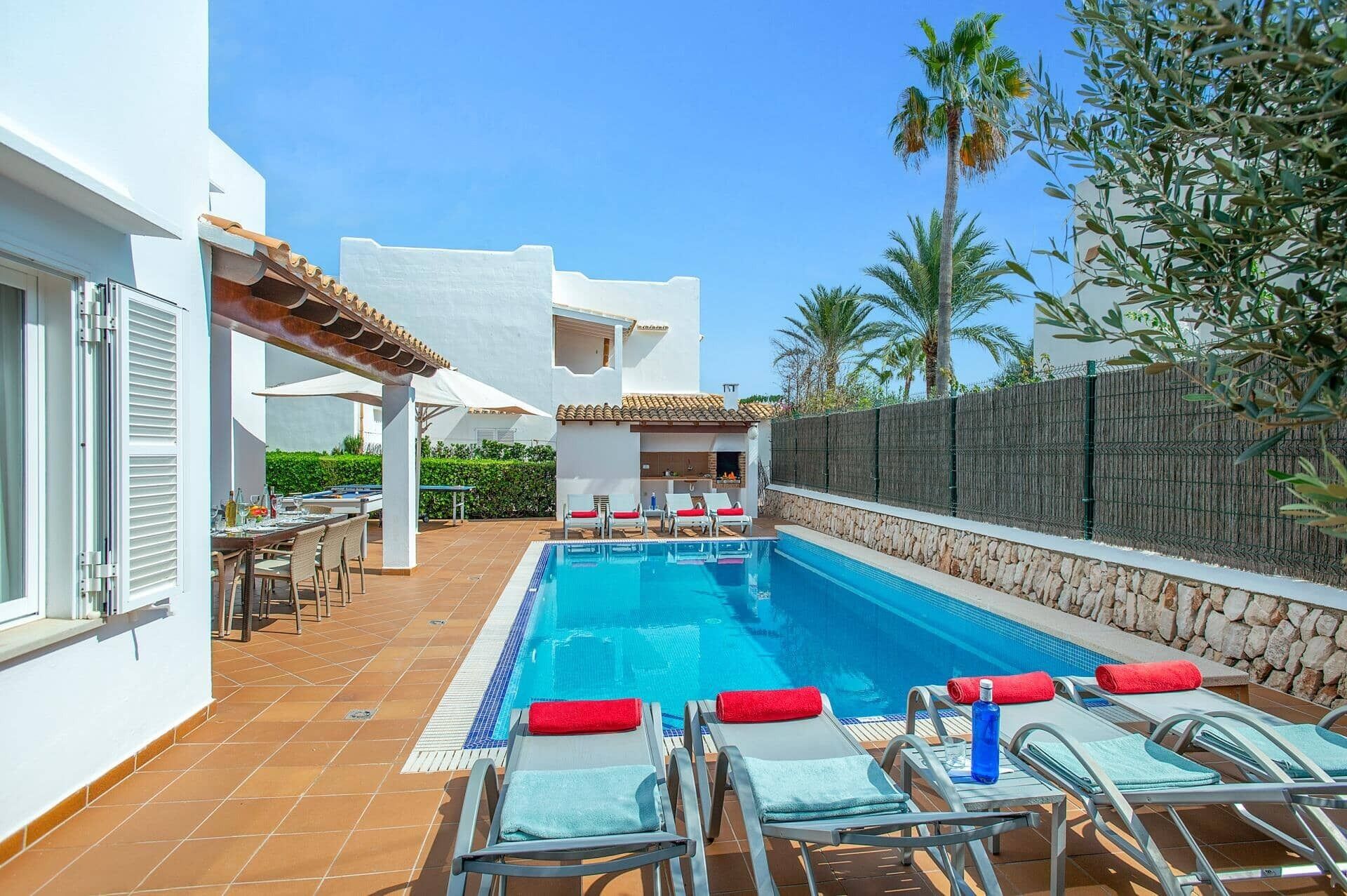 A poolside area with lounge chairs, a dining setup, and a stone wall.