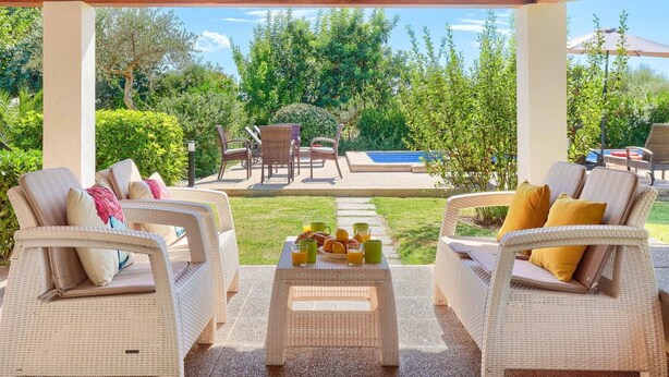 A covered outdoor seating area with wicker furniture and a pool in the background. - Villa Garriguer by Villa Plus (Mallorca)