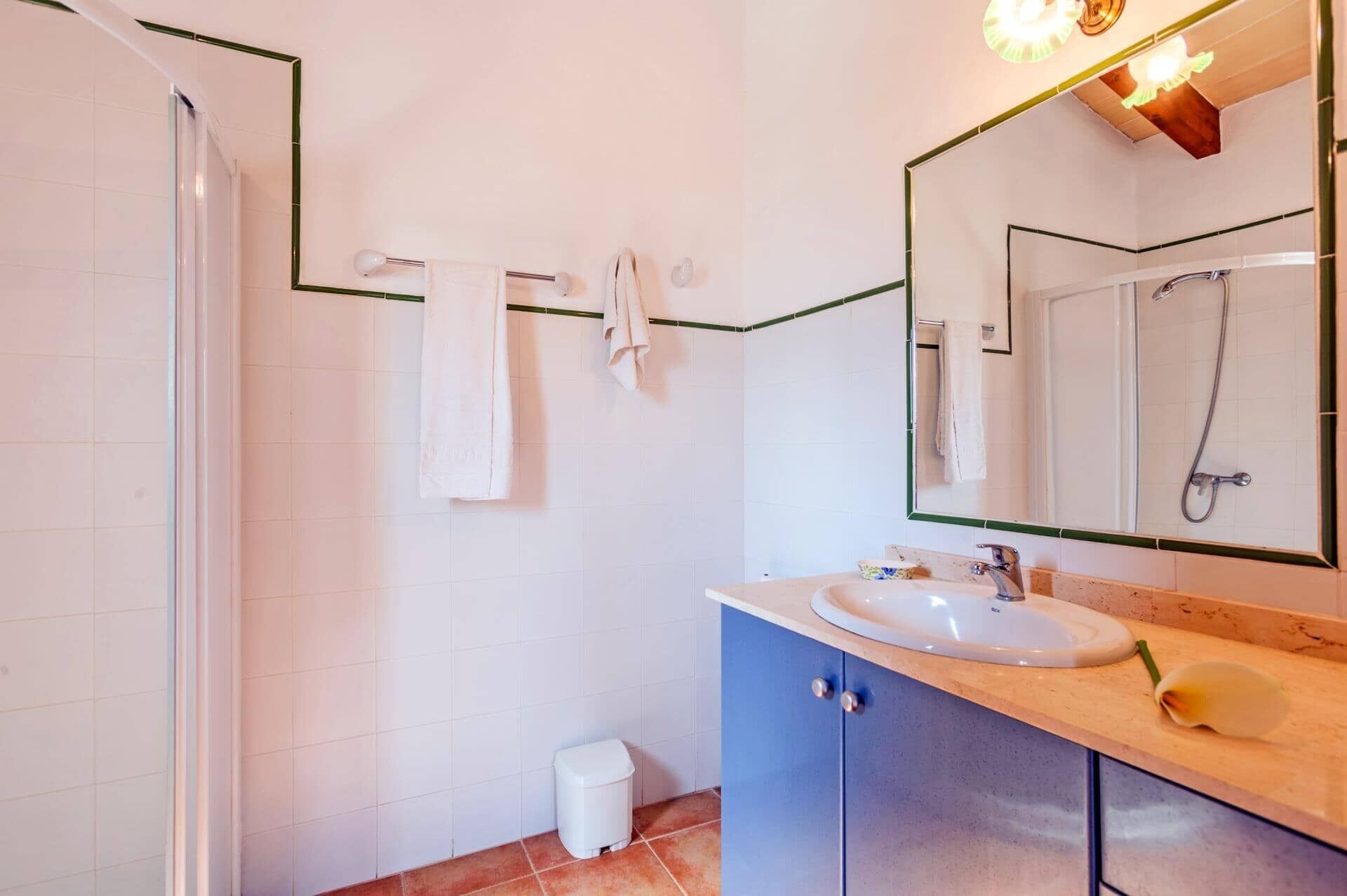 Une salle de bain moderne avec des carreaux blancs, un meuble bleu, un lavabo, une douche et un miroir avec éclairage.