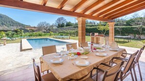 An outdoor dining area with a pool, wooden pergola, and a view of the countryside.