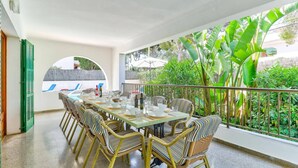 A covered outdoor dining area with a table set for six, surrounded by wicker chairs with striped cushions.