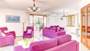 A spacious living room with purple sofas, a coffee table with breakfast items, a chandelier, and a painting on the wall.