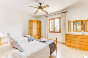 A bedroom with a bed, a wooden wardrobe, a dresser, a ceiling fan, and a window with curtains.