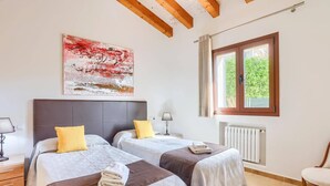 Ett hotellrum med två sängar, ett element, ett fönster med gardiner, en tavla på väggen och en stol.