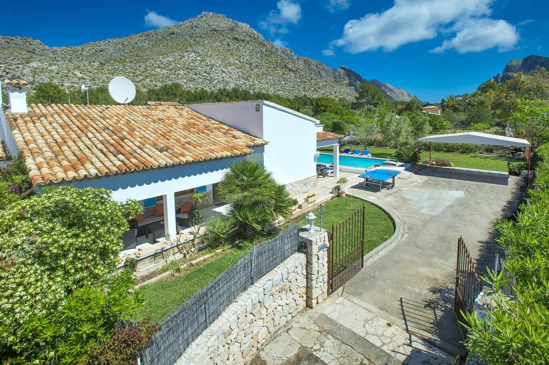 A villa with a tiled roof, a swimming pool, and a stone wall.