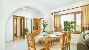 Un coin repas avec une table en bois, dressée pour quatre personnes et entourée de chaises, offrant une vue sur la verdure à l’extérieur.