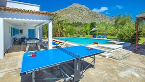 Un espace piscine comprenant deux tables de ping-pong, une piscine et une montagne en arrière-plan.