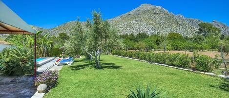 A well-maintained lawn with a swimming pool, a mountain in the background, and a clear blue sky.