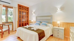 Une chambre à coucher comprenant un lit, des tables de chevet, une chaise, une armoire en bois et une fenêtre avec des rideaux.