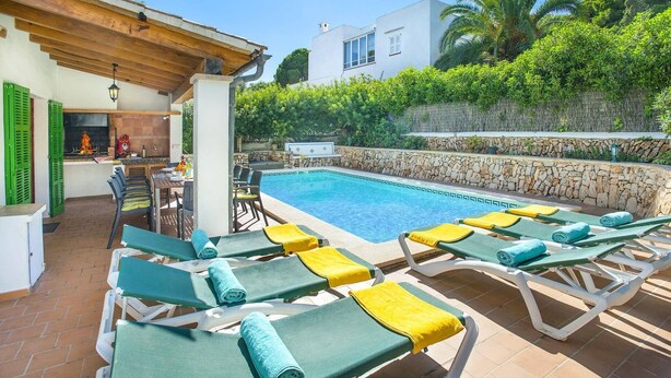 A poolside area with lounge chairs, a barbecue setup, and a stone wall. - Villa Malen by Villa Plus (Cala d'Or)