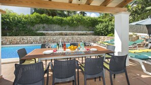 An outdoor dining area with a pool view, stone wall, and greenery. - Villa Malen by Villa Plus (Cala d'Or)