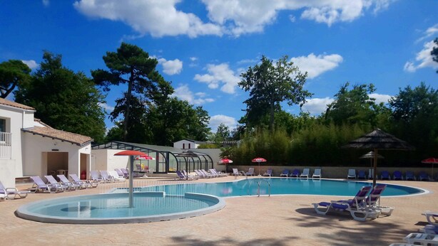 A swimming pool with sun loungers and umbrellas, surrounded by trees and buildings.