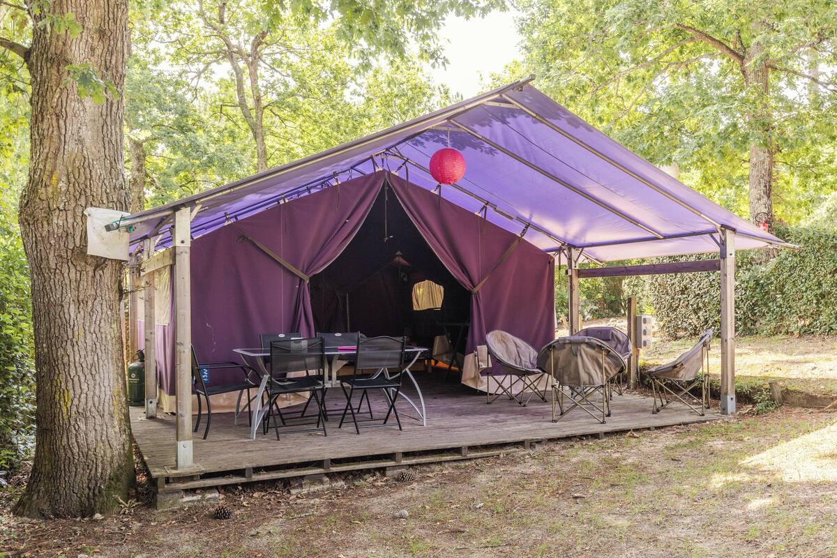 A tent with a table and chairs, surrounded by trees.