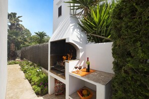 An outdoor barbecue area with a white chimney, a bottle of wine, and a bowl of fruit. - Villa Roig by Villa Plus (Cala d'Or)
