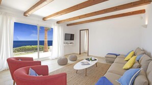 Ein Wohnzimmer mit einem großen Fenster mit Blick auf den Ozean, einer Couch mit Kissen, einem Couchtisch und roten Sesseln.