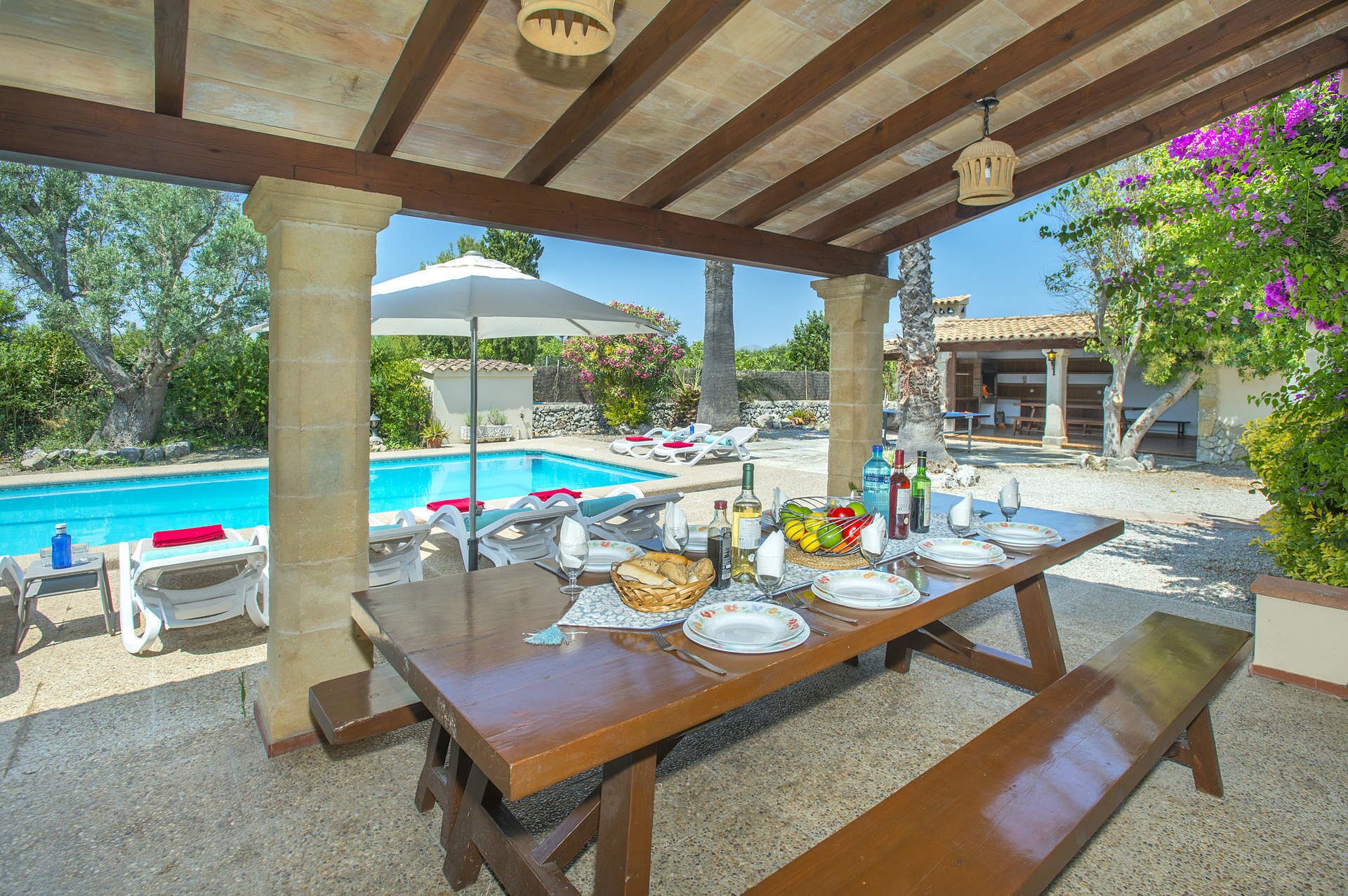 Ein Essbereich im Freien mit Blick auf einen Pool, einer Holz-Pergola und Liegestühlen.