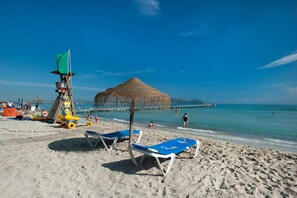 A beach with sun loungers, a lifeguard tower, and a thatched structure. - Villa Sebastian by Villa Plus (Mallorca)