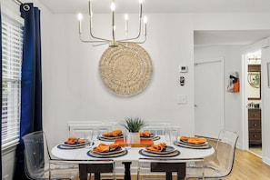 A dining area with a round table, clear chairs, a woven wall hanging, and a modern chandelier.