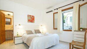 A hotel room with a bed, bedside tables, a window with curtains, a small table with a plant, and a chair. - Villa Sol Pollensa by Villa Plus (Mallorca)