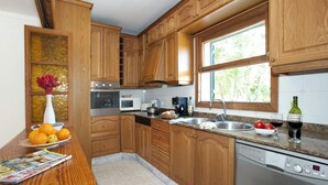 A kitchen with wooden cabinets, a stainless steel sink, a dishwasher, and a window providing natural light. - Villa Sol Pollensa by Villa Plus (Mallorca)