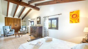 A bedroom with a bed, a dresser, a chair, and a window with curtains. - Villa S'Olivellas by Villa Plus (Mallorca)