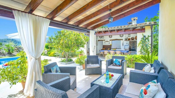 A covered outdoor seating area with wicker furniture, a pool, and a kitchen in the background. - Villa S'Olivellas by Villa Plus (Mallorca)