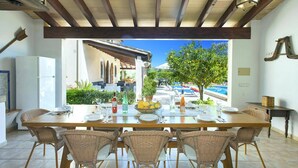 A dining area with a table set for six, surrounded by wicker chairs, overlooking a pool and garden. - Villa S'Olivellas by Villa Plus (Mallorca)