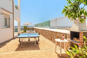 Un patio al aire libre con mesa de ping pong, una parrilla y un muro de piedra.