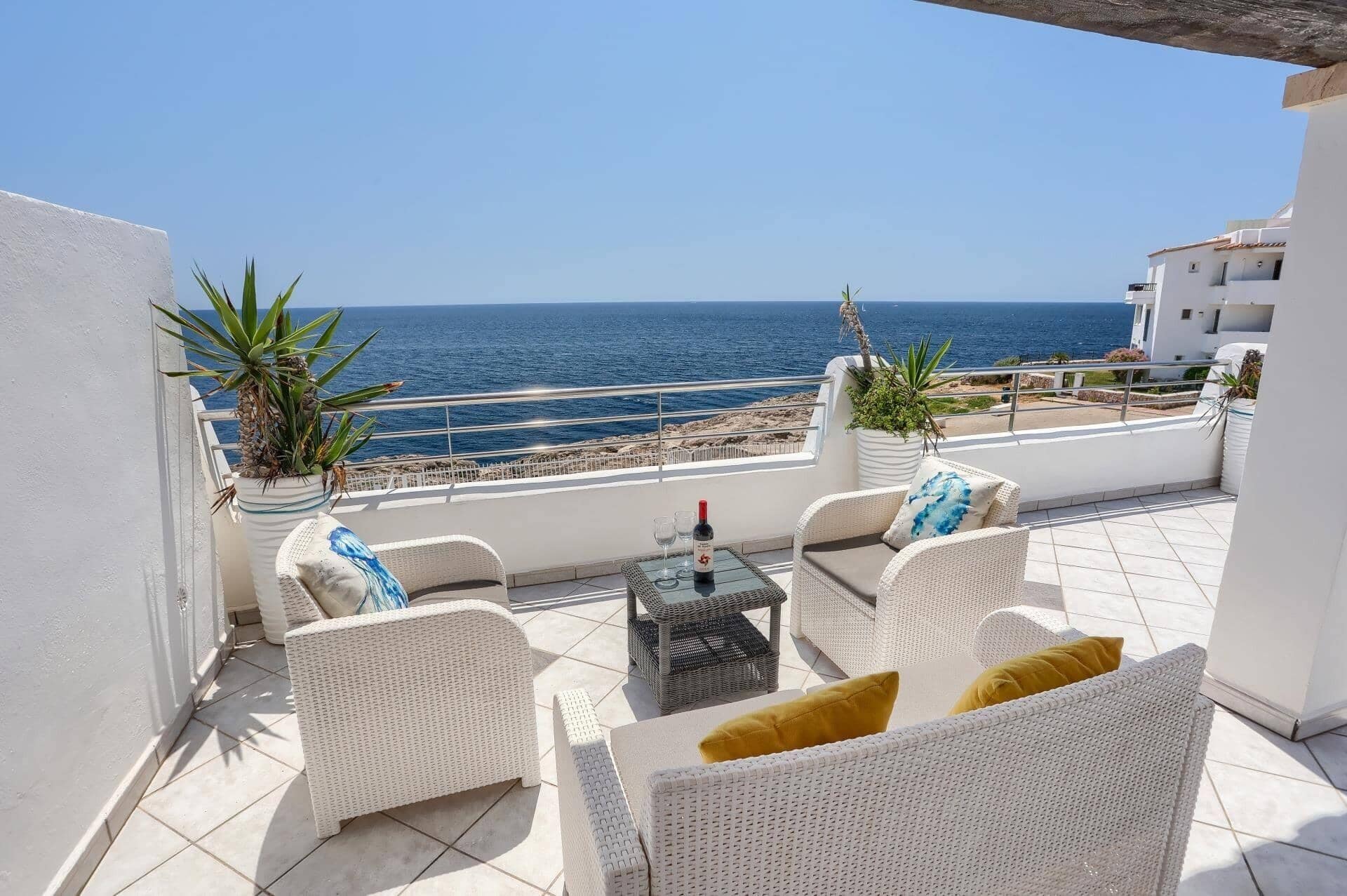 A terrace with wicker furniture, a table with a bottle and glasses, and a view of the sea.