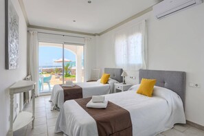Une chambre d’hôtel avec deux lits, un balcon offrant une vue agréable et une décoration aux tons blancs.