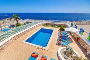 Un espace piscine avec vue sur la mer, entouré de chaises longues et d’une clôture blanche.
